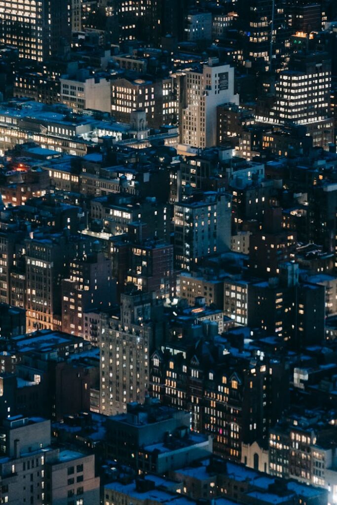 From above of modern tall houses with bright glowing lights located on dark streets of contemporary megapolis at night time